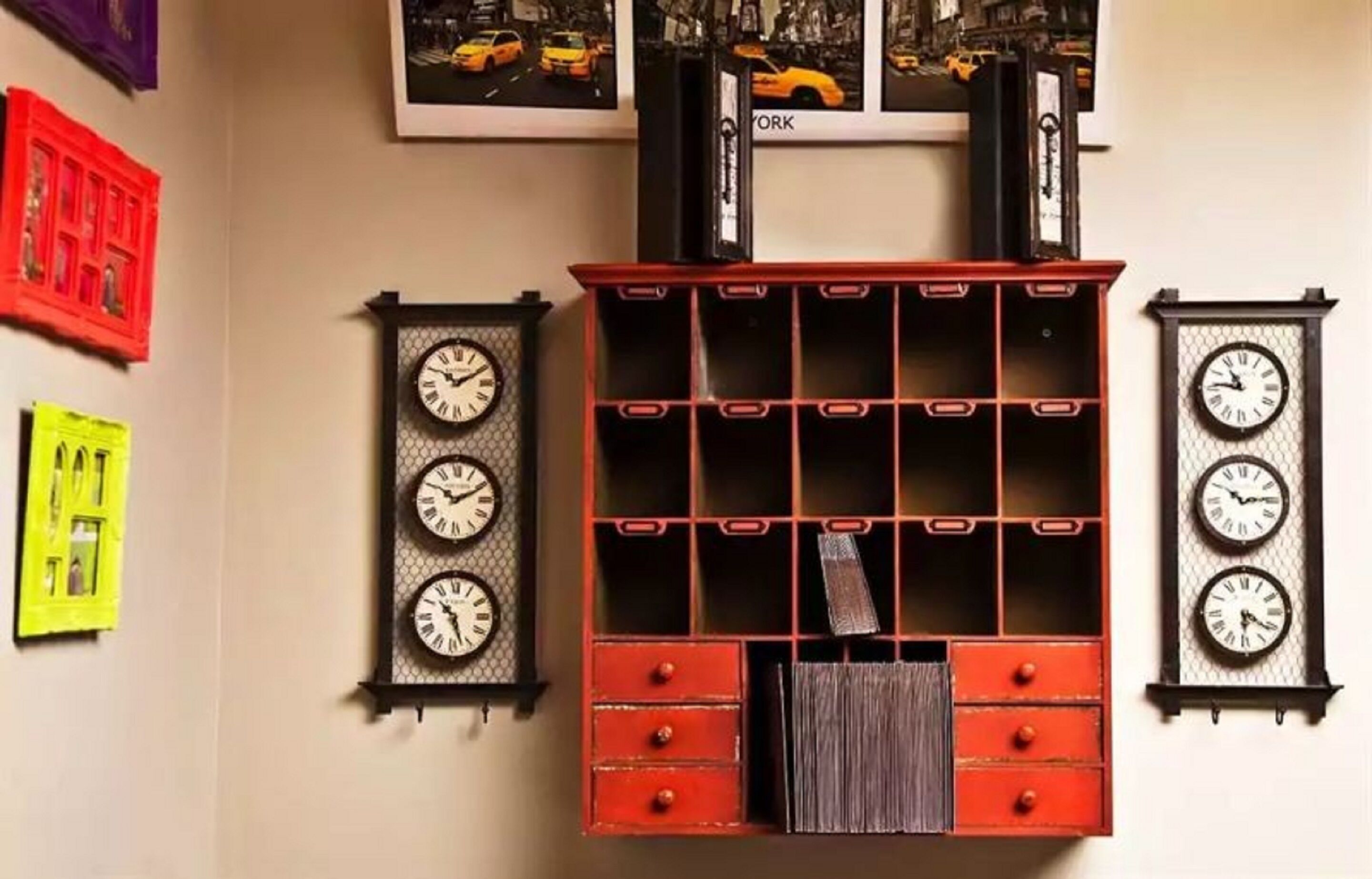 Una pared con tres relojes, un mueble de almacenamiento rojo y un cuadro con taxis.