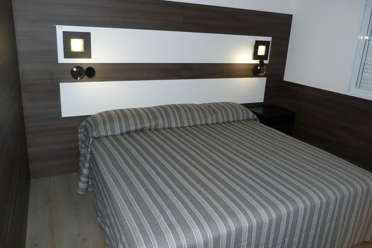 A bedroom with a bed, a headboard with integrated lighting, and a bedside table.