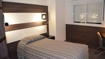 Un dormitorio con cama, mesita de noche, silla, ventana y cabecero con luz.