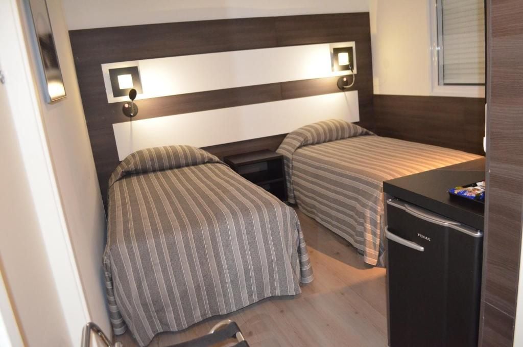 Habitación compacta con dos camas, una kitchenette pequeña y un banco empotrado.