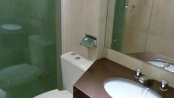 Un baño con inodoro, lavamanos, espejo y cabina de ducha de vidrio.