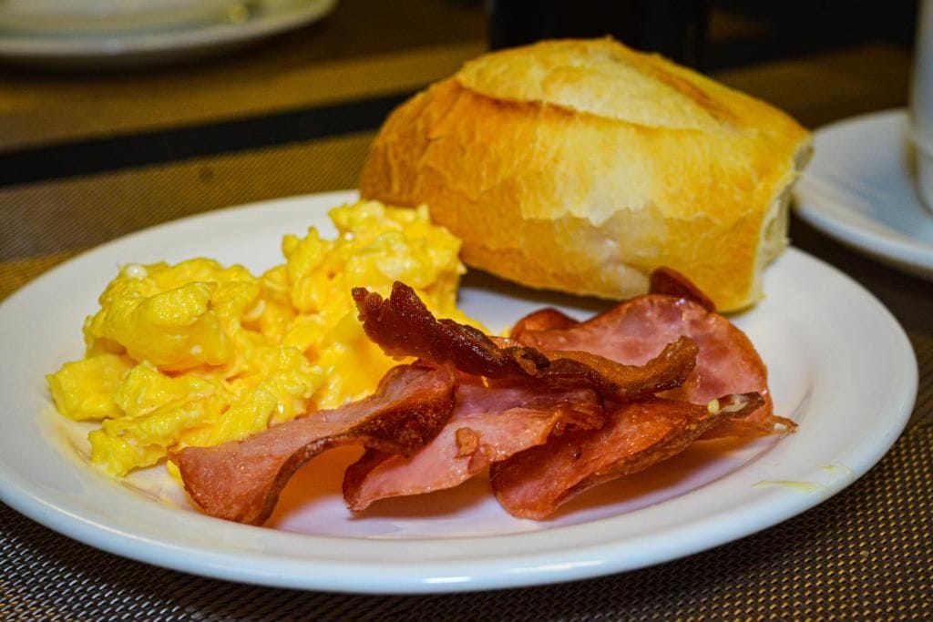Un plato con huevos revueltos, tocino y un croissant.