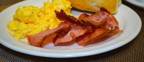 Un plato con huevos revueltos, tocino y un croissant.