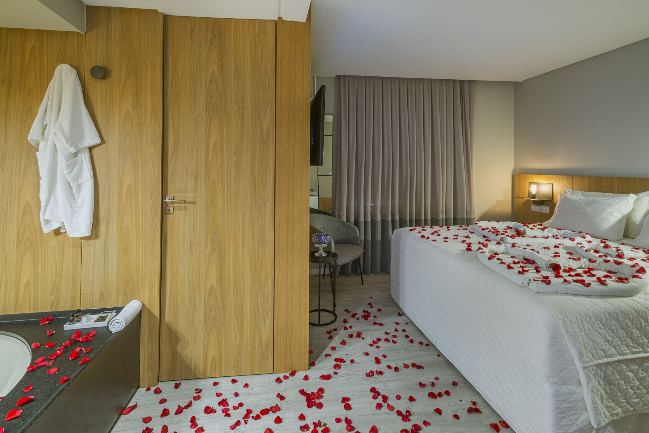 A hotel room with a bed, a desk, a chair, a bathroom, and a wooden wardrobe.