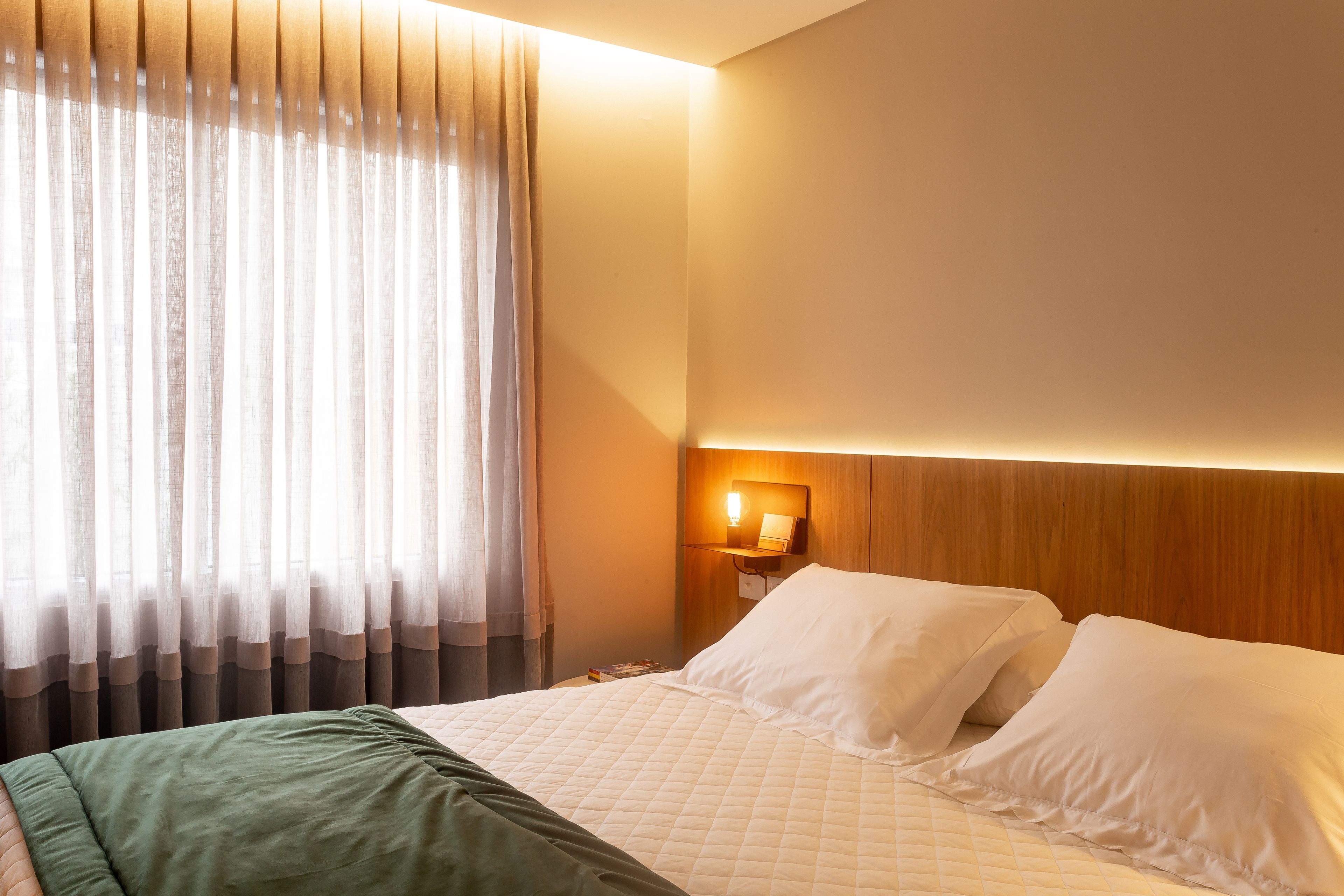 A hotel room with a bed, a nightstand, a lamp, and a window with curtains.