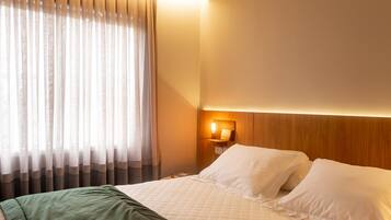 Una habitación de hotel con cama, mesita de noche, lámpara y ventana con cortinas.