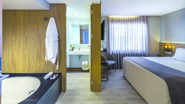 A hotel room with a large bed, a separate bathroom with a bathtub, a desk, and a chair. - Hotel Melo (Balneário Camboriú)