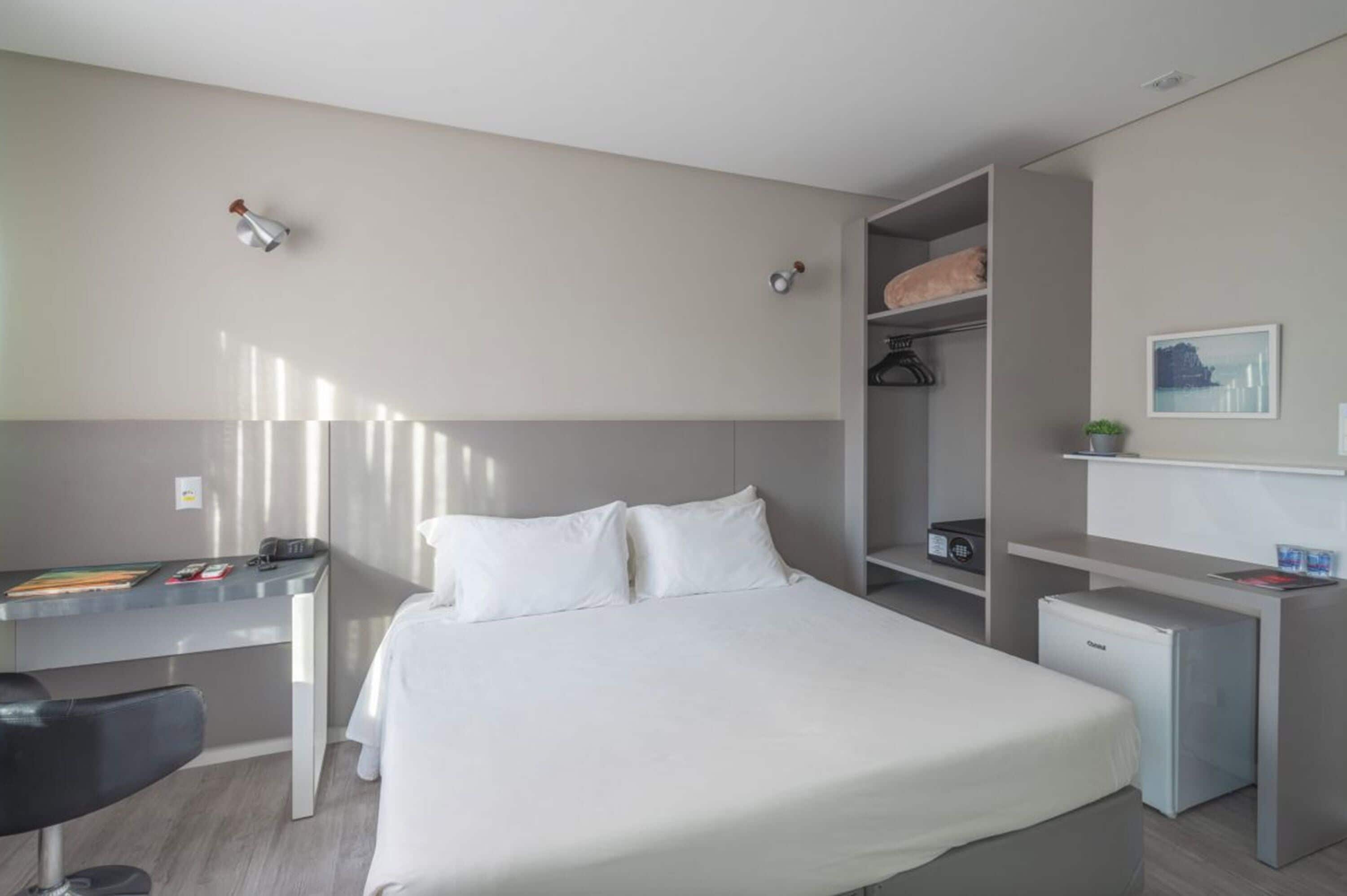 Una camera d'albergo moderna con un letto, una scrivania, un piccolo frigorifero e un armadio.