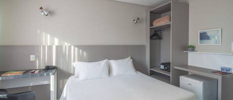 Una camera d'albergo moderna con un letto, una scrivania, un piccolo frigorifero e un armadio.