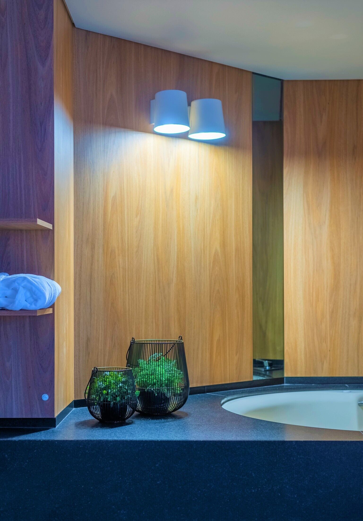 Une salle de bain moderne avec un lambris en bois, un lavabo rond et deux paniers en métal noir ornés de plantes vertes.