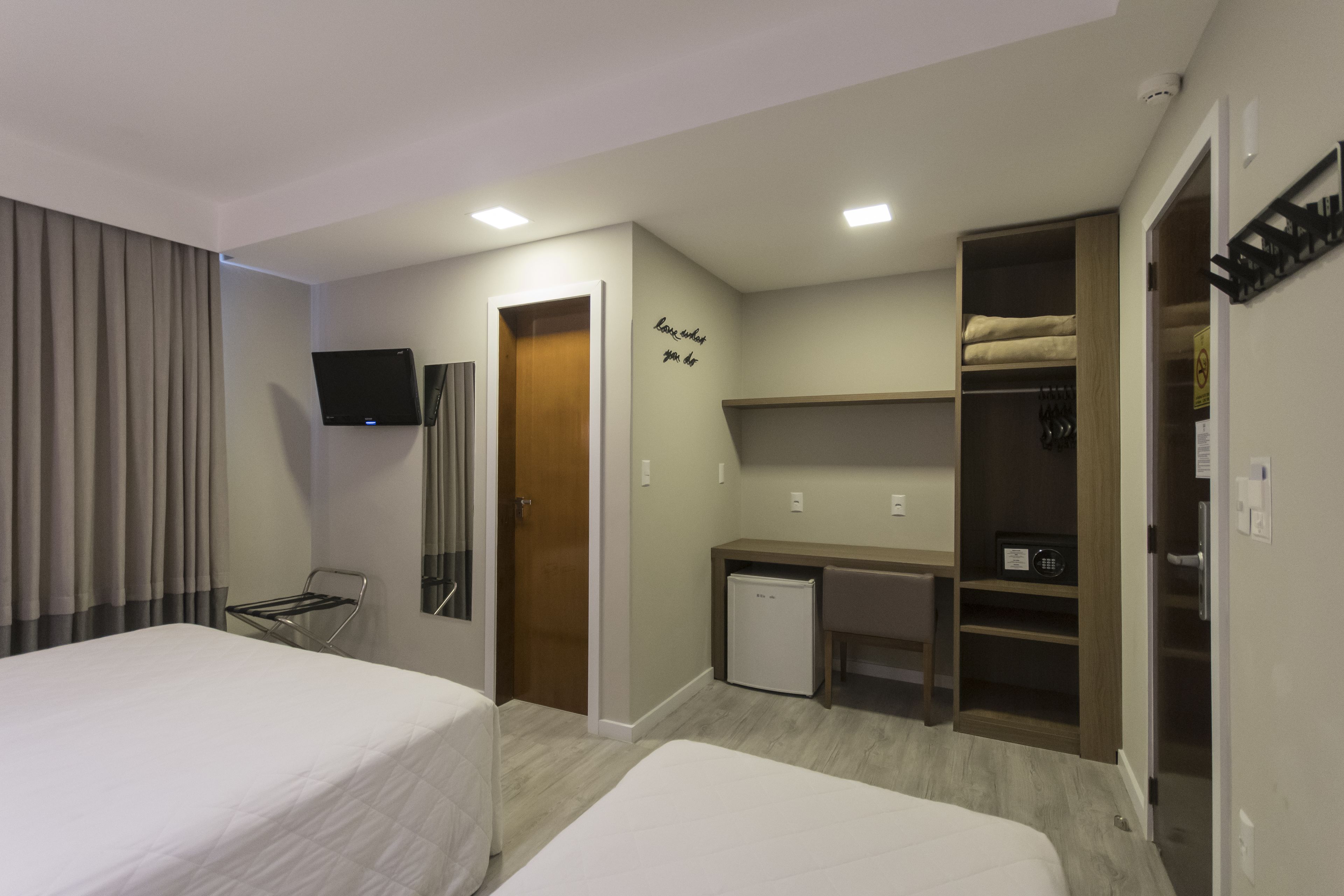 A hotel room with two beds, a desk, a small refrigerator, a TV, and a wardrobe.