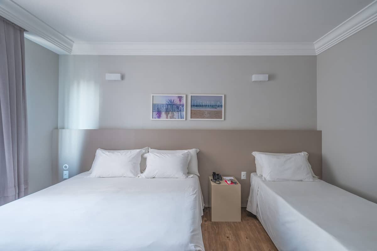 A hotel room with two beds, a bedside table with a phone and a book, and two wall-mounted artworks.