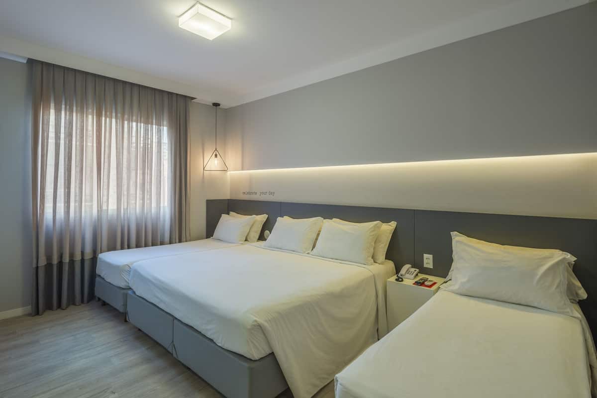 A hotel room with two beds, a bedside table with a phone, and a wall-mounted light fixture.