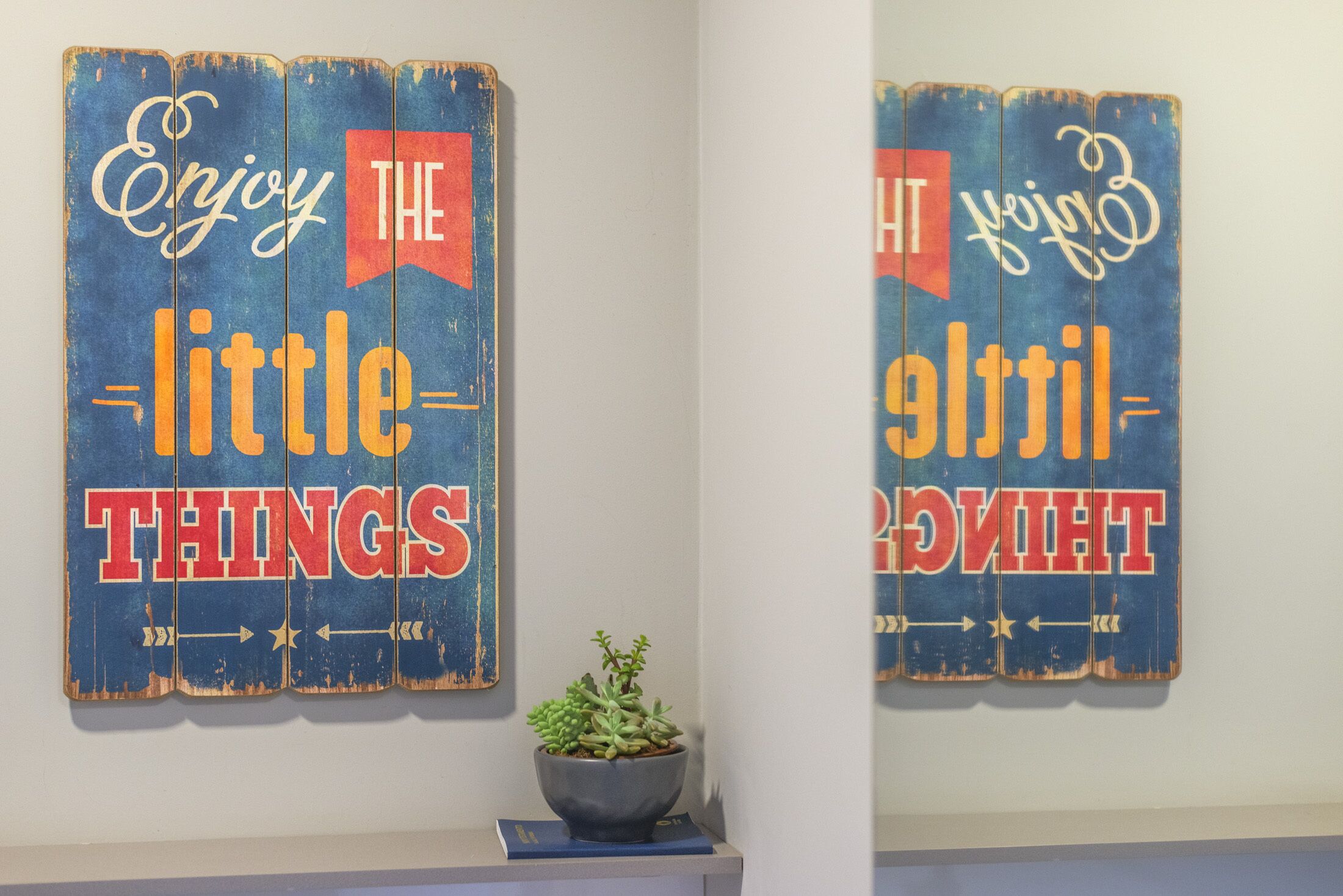 Two wall-mounted signs with the text "Enjoy the little things" and "Light the way" in a rustic design.