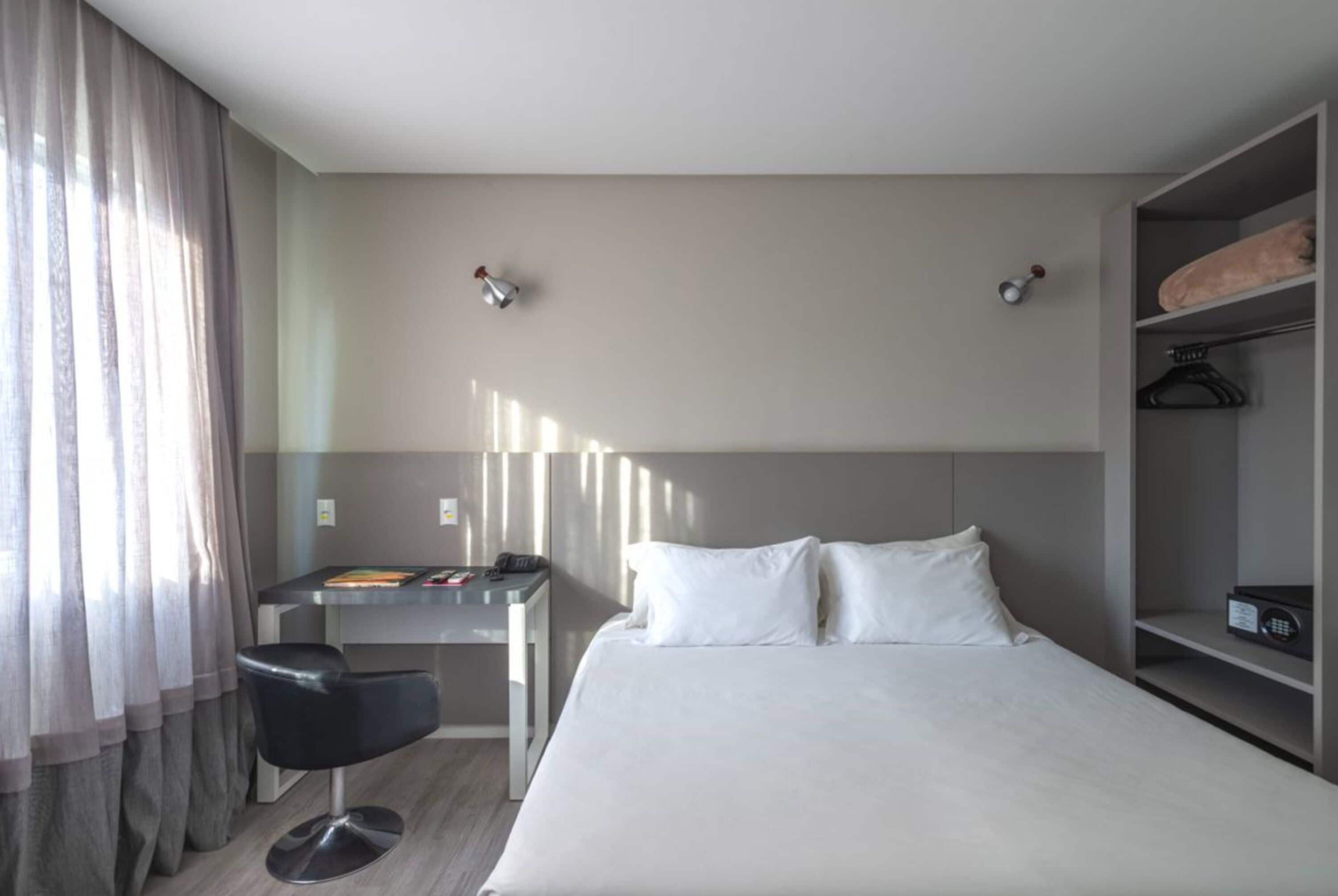 Habitación de hotel con cama, escritorio, silla y armario.