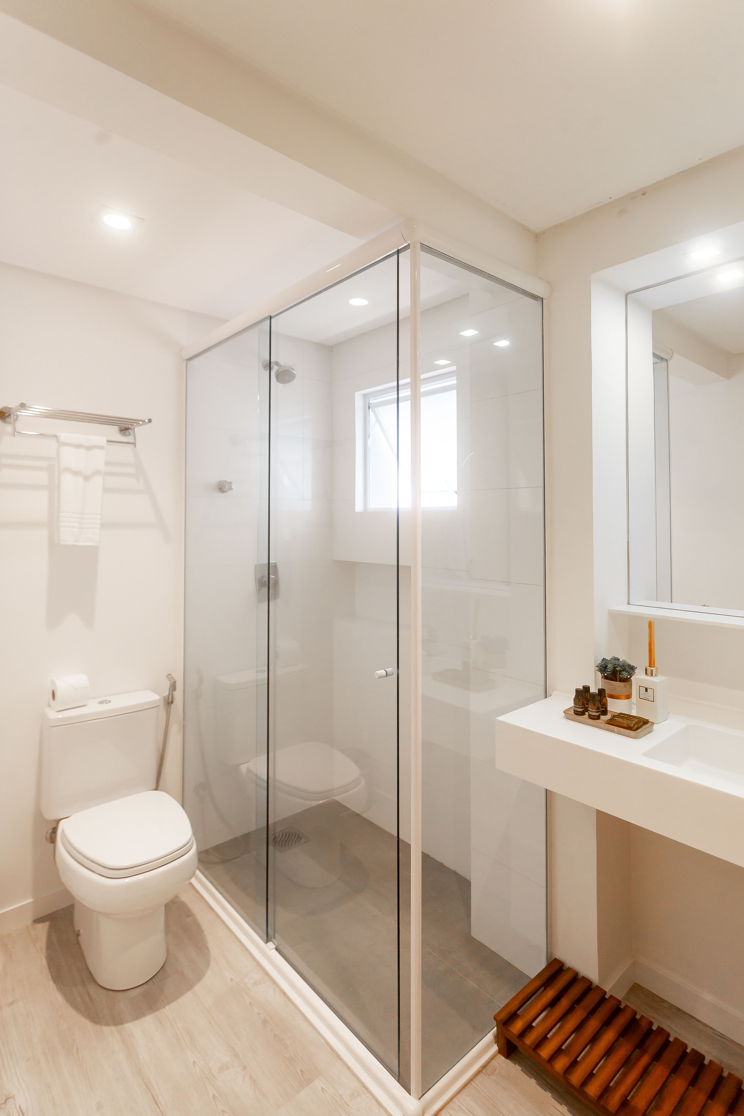 Een moderne badkamer met een douche met glazen wand, een wit toilet en een witte wastafel met een spiegel erboven.