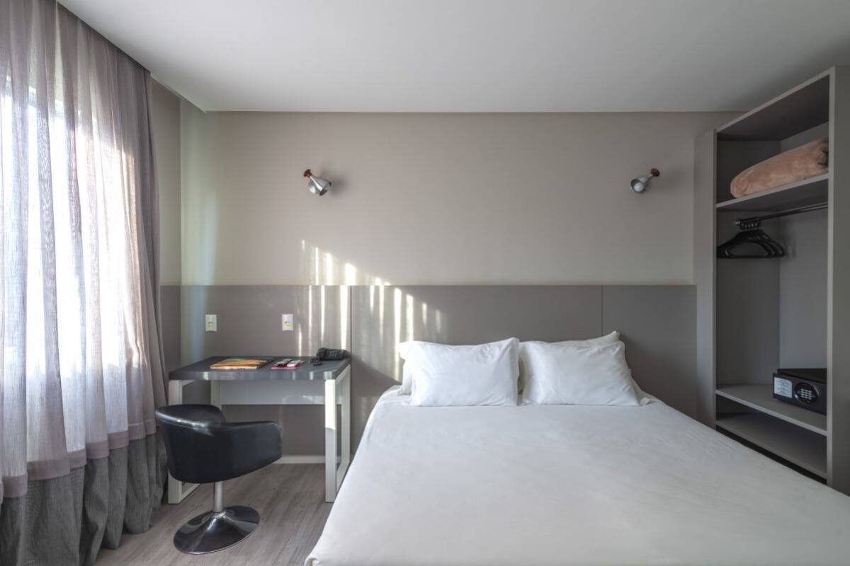 A hotel room with a bed, a desk, a chair, and a wardrobe.