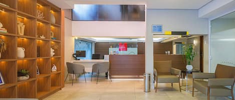 A hotel reception area with a wooden reception desk, seating area, and a large window overlooking the street.