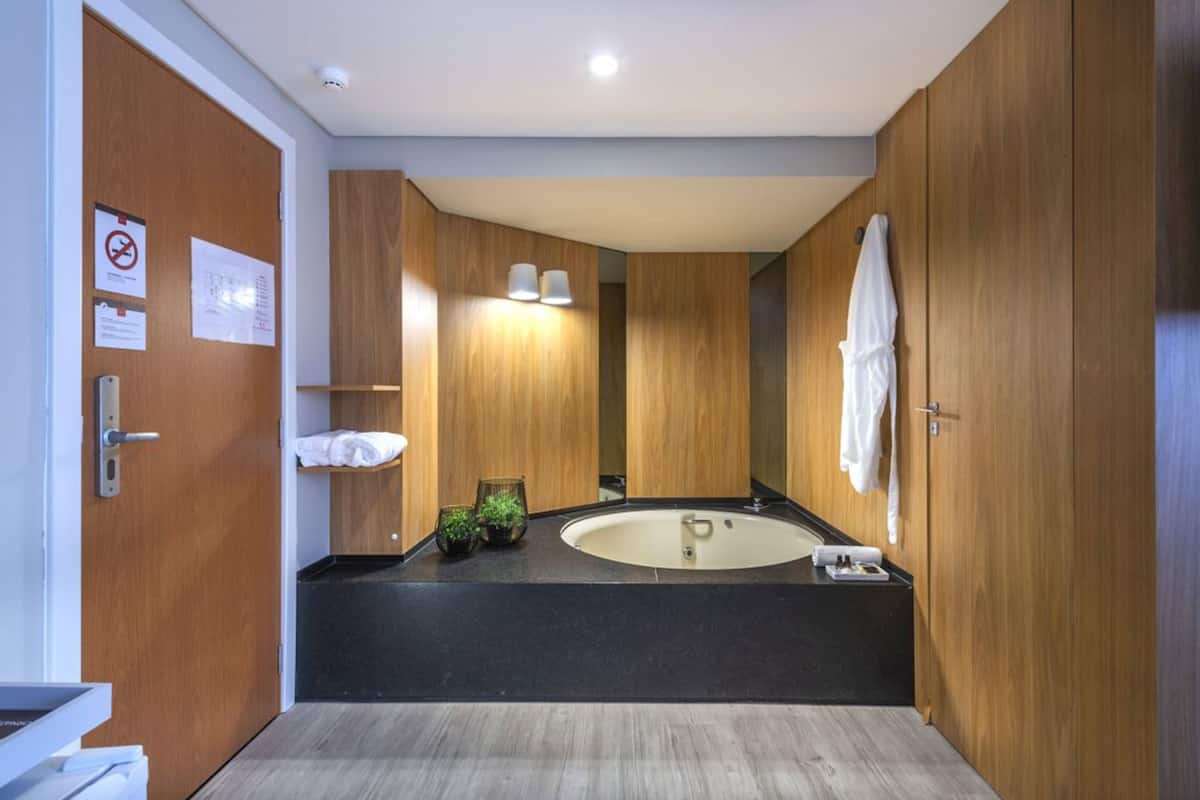 A modern bathroom with a large bathtub, wooden cabinetry, and a black countertop.