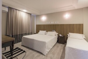 A hotel room with two beds, a desk, a chair, a telephone, and a wall-mounted light.