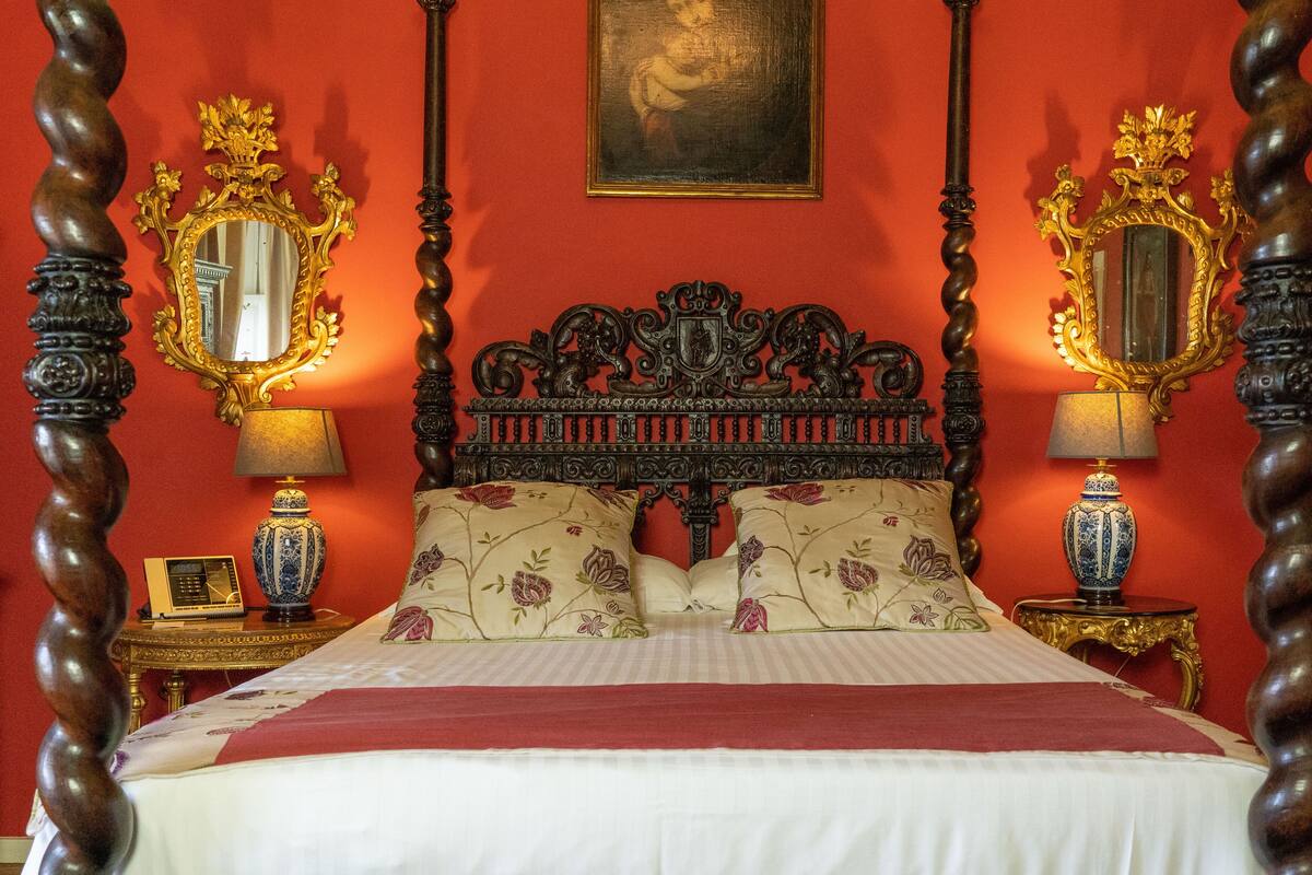 A bed with a red headboard, two ornate mirrors, and floral pillows.