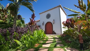 A white building with a red door and a circular window, surrounded by lush tropical plants and a stone pathway. - Hotel Hacienda de Abajo - Adults Only (Tazacorte)