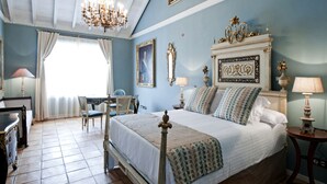 A bedroom with a bed, a chair, a desk, a chandelier, and a window with curtains.