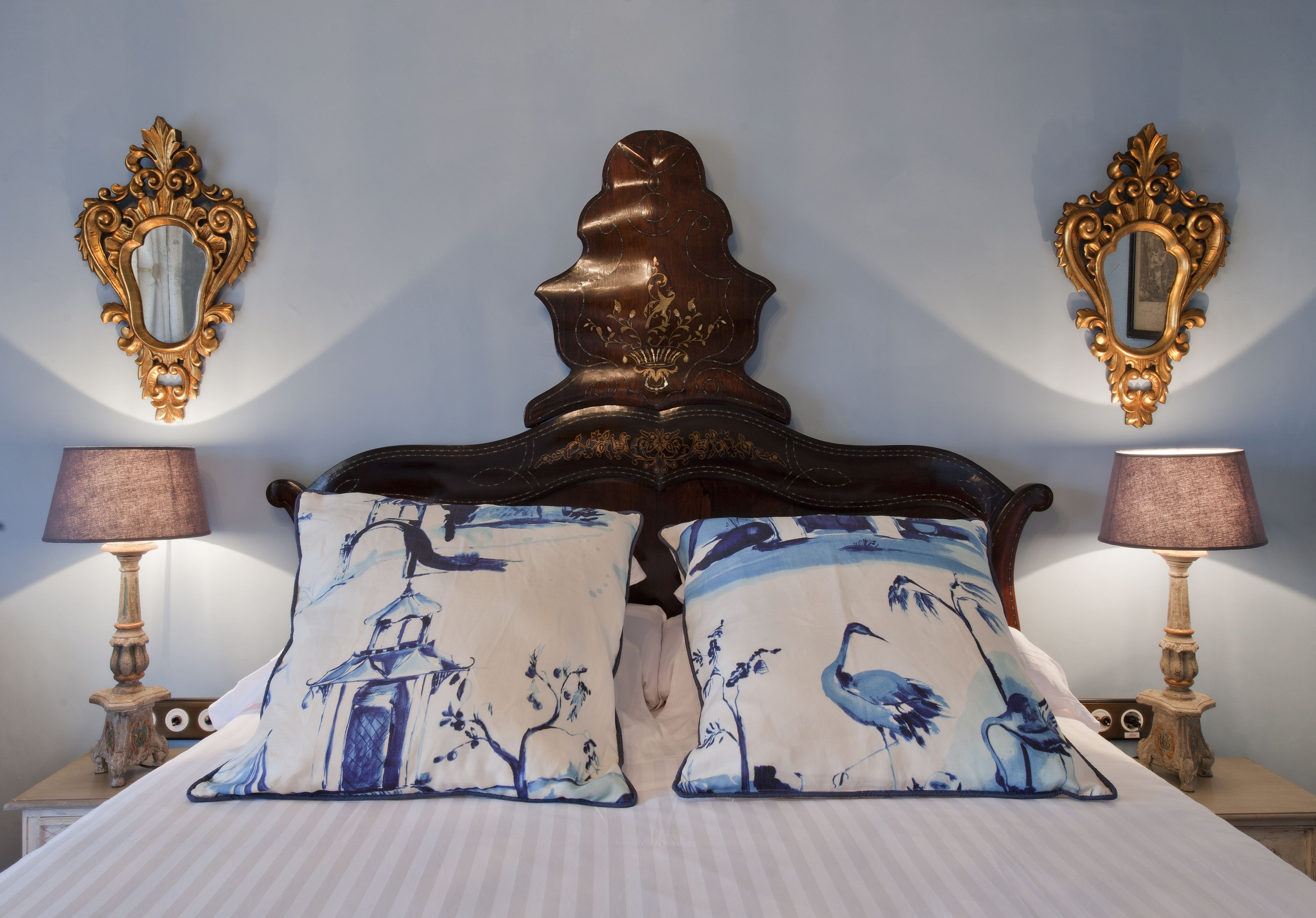 Una cama con un cabecero decorado, dos lámparas a juego y almohadones con diseños de pájaros.