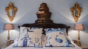 Una cama con un cabecero decorado, dos lámparas a juego y almohadones con diseños de pájaros.