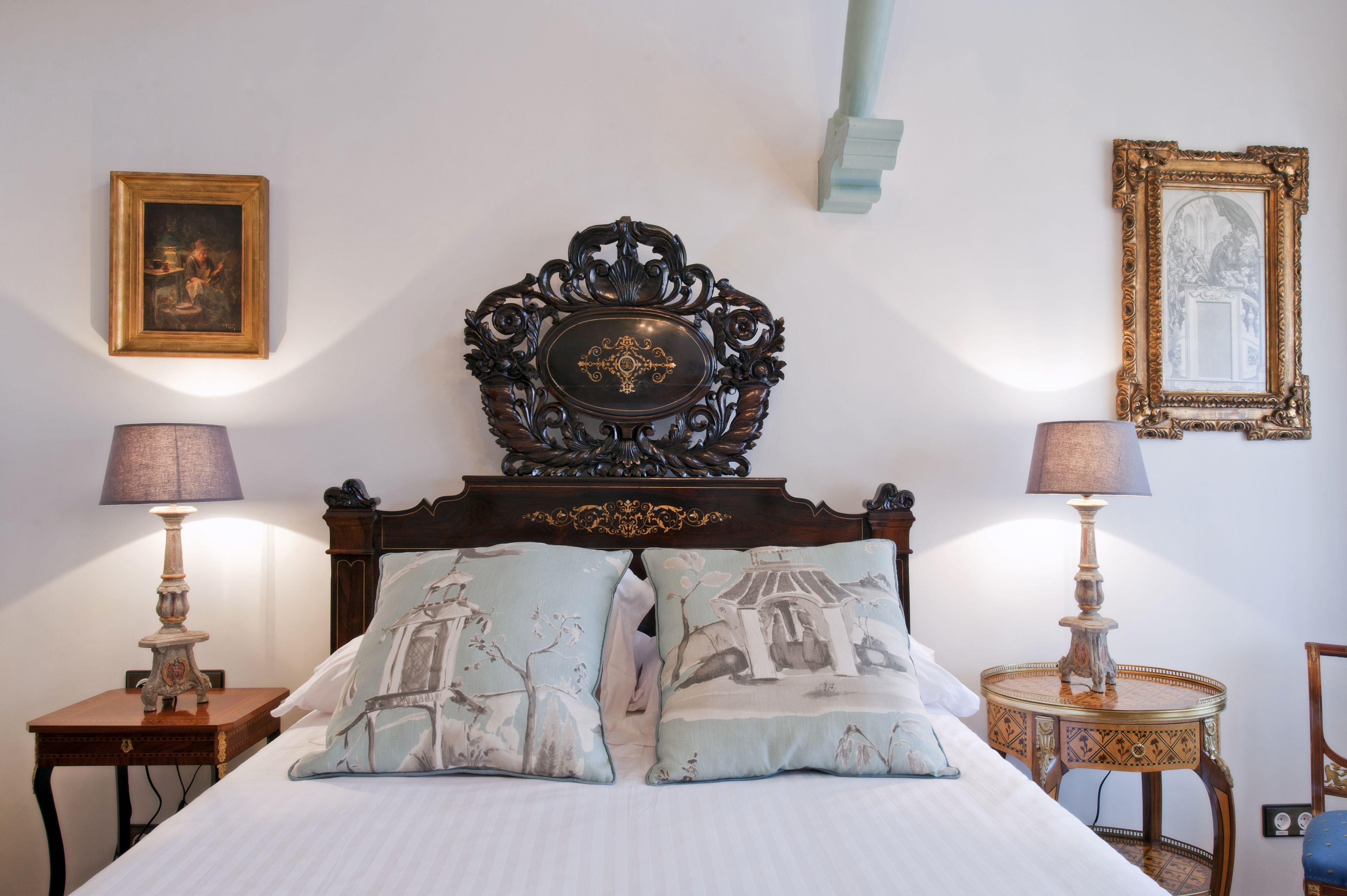 A bedroom with a wooden headboard, two bedside tables with lamps, a bed with patterned pillows, and framed artwork on the walls.