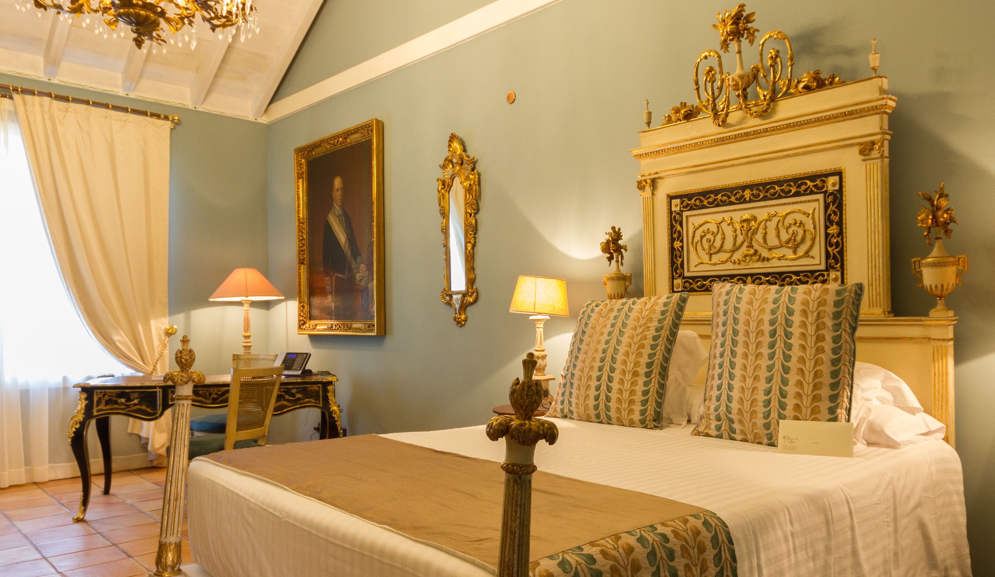 Une chambre à coucher avec un grand lit, deux tables de chevet, un lustre et un tableau au mur.