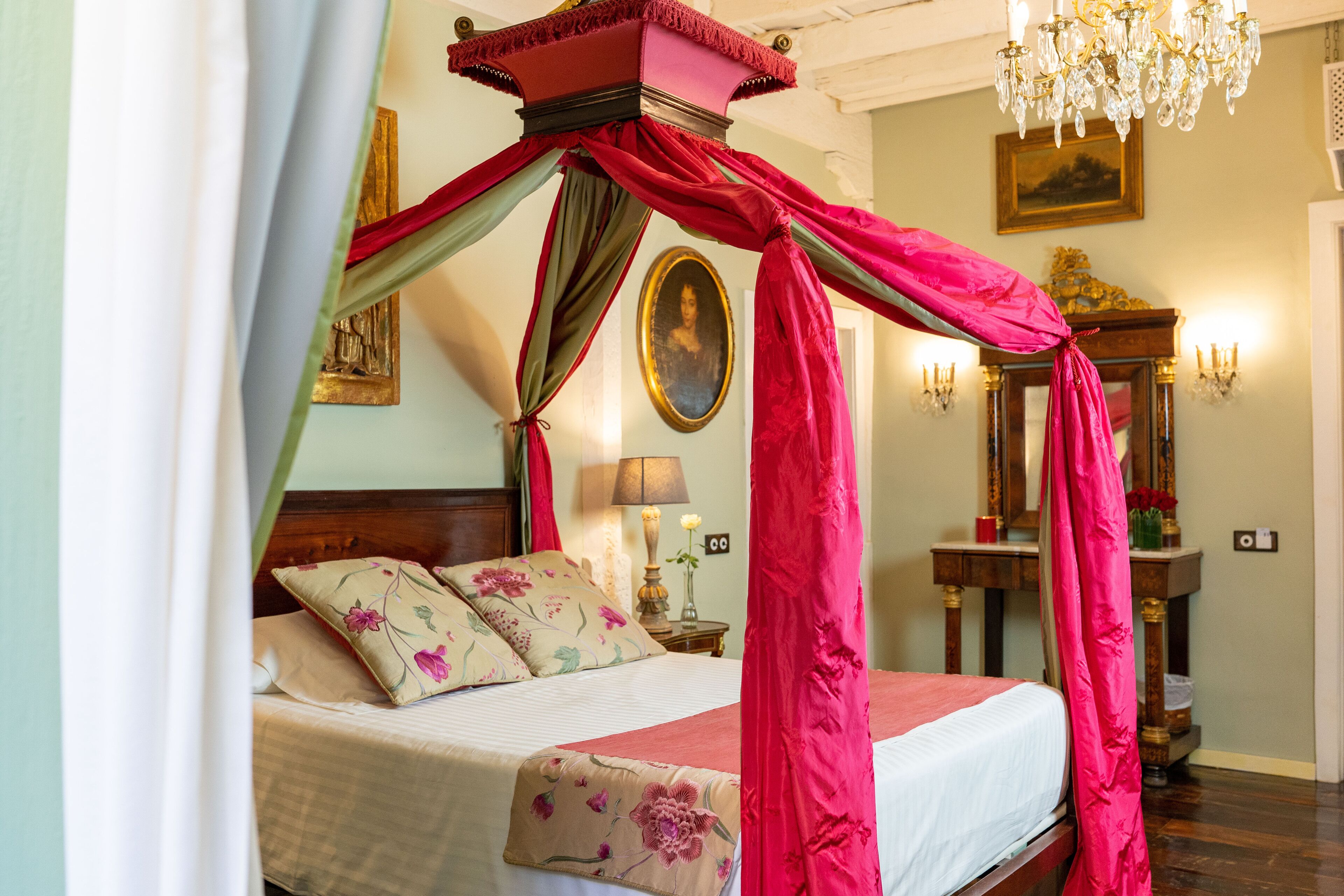 A bedroom with a four-poster bed, a chandelier, and a mirror.