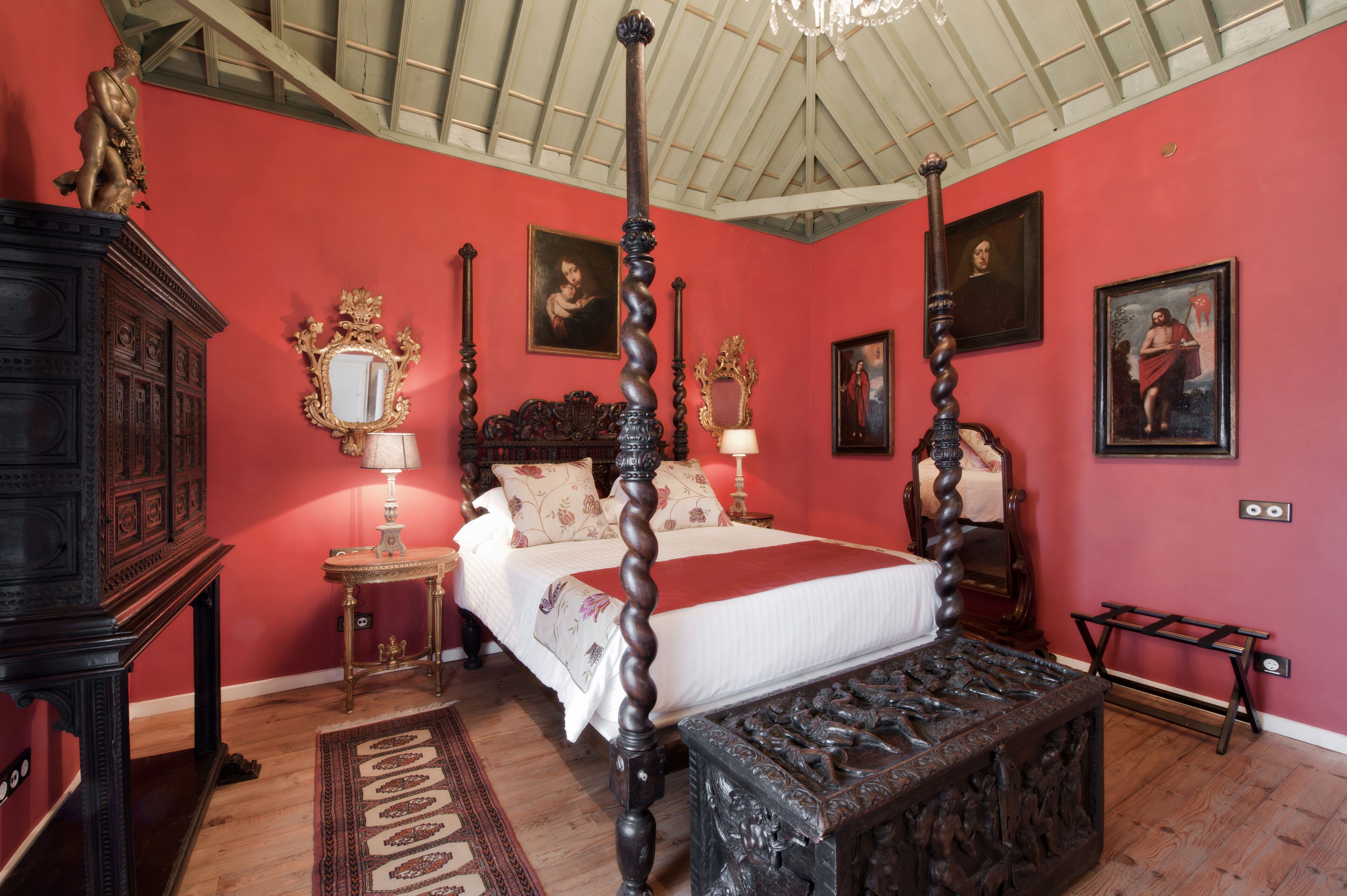 A bedroom with a four-poster bed, a wooden cabinet, a mirror, and artwork on the walls.