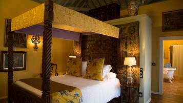 A four-poster bed with floral bedding, a nightstand with a lamp, and a vintage-style bathroom with a clawfoot tub.