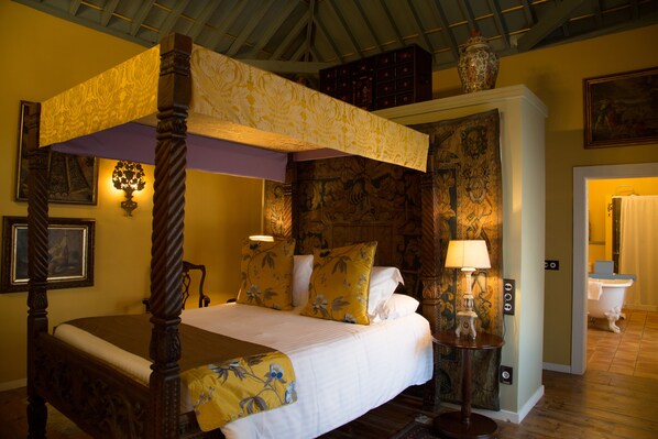 Una cama con dosel y ropa de cama floral, una mesita de noche con lámpara, y un baño de estilo antiguo con bañera tipo pata de león.