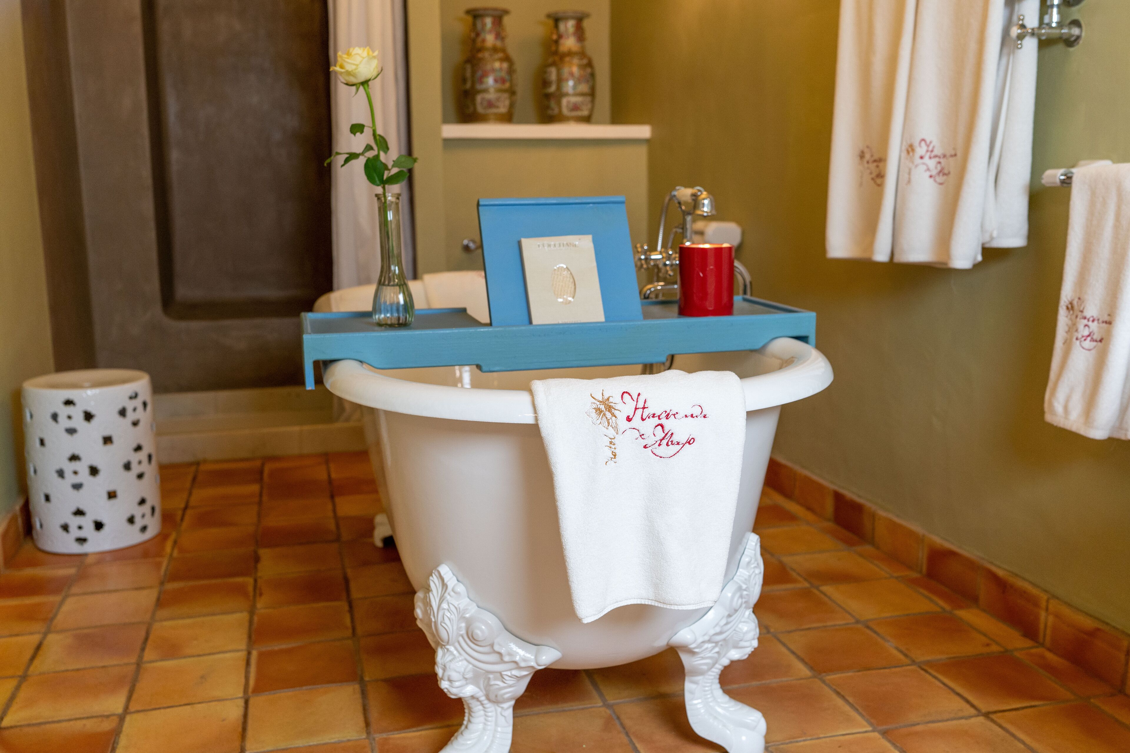 A bathroom with a bathtub, a towel rack, a vase with a flower, and a framed picture on the edge of the tub.