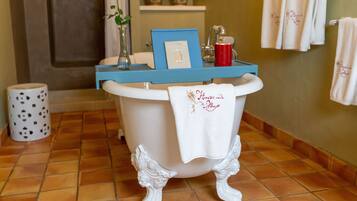 A bathroom with a bathtub, a towel rack, a vase with a flower, and a framed picture on the edge of the tub.