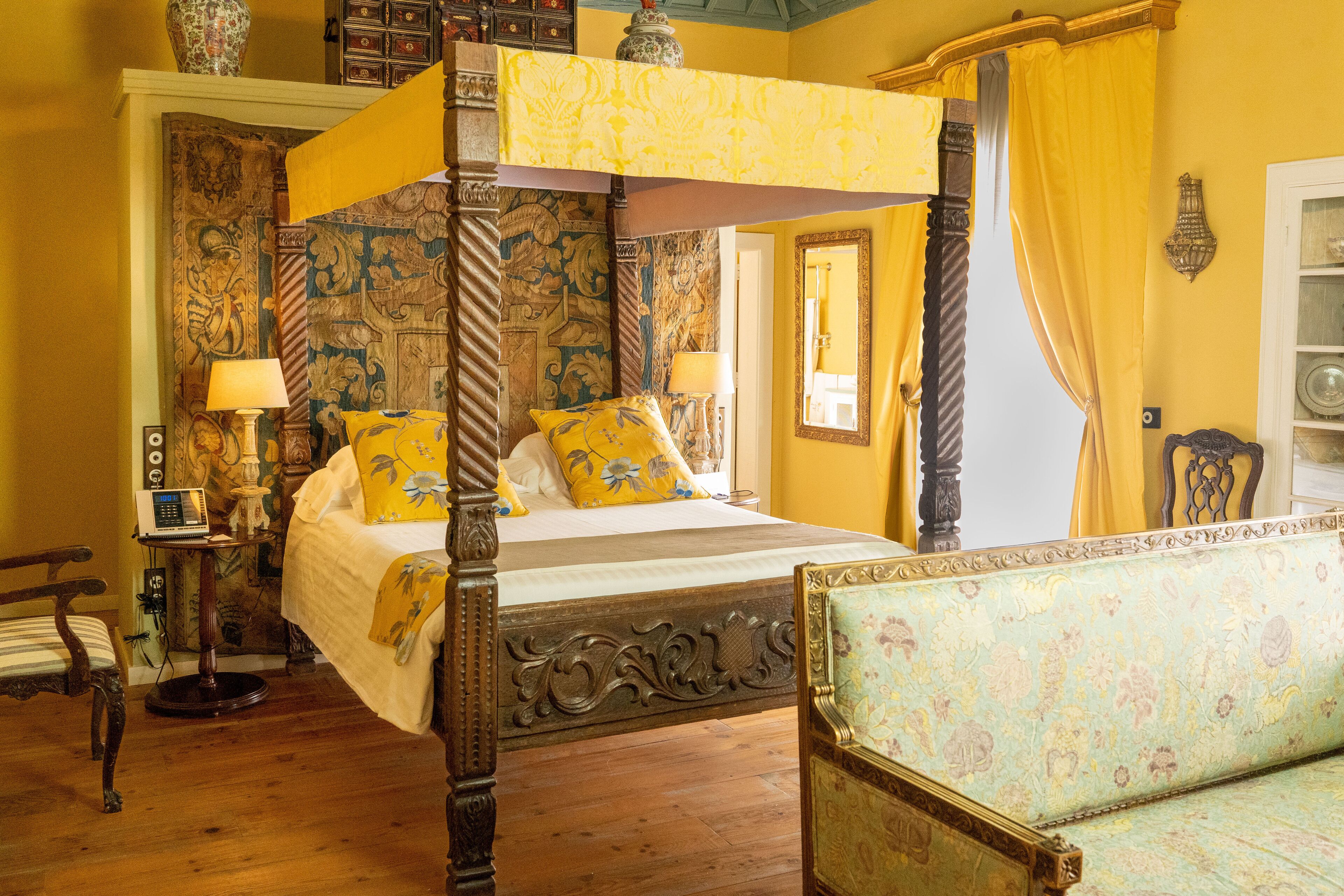Ein Himmelbett mit Baldachin, ein Sofa mit Blumenmuster und ein Holzboden.
