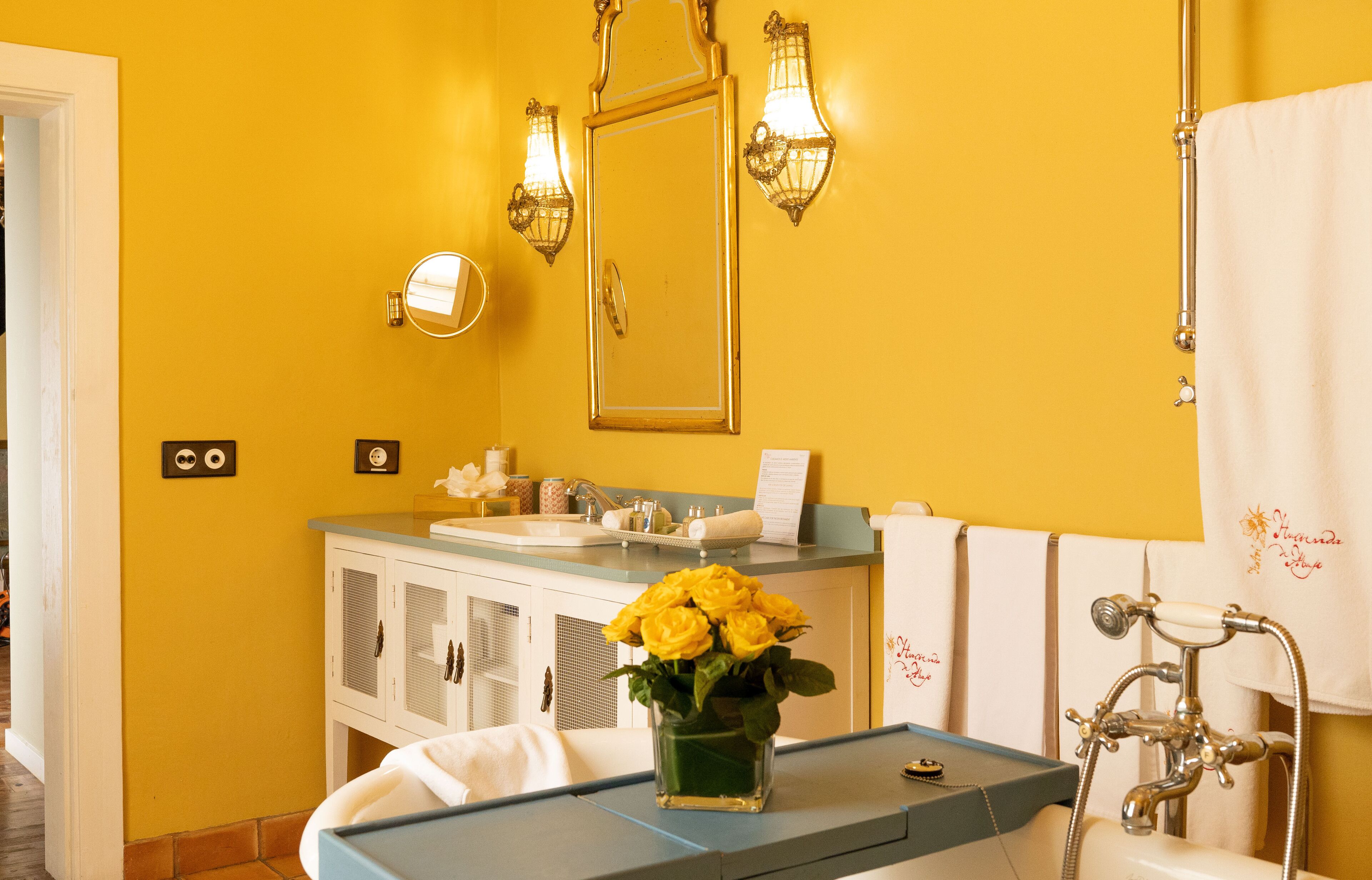A bathroom with a yellow wall, a sink, a mirror, and a vintage-style shower.