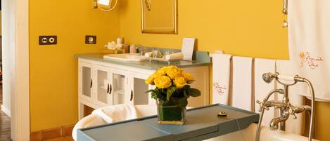 A bathroom with a yellow wall, a sink, a mirror, and a vintage-style shower.
