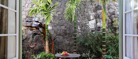 Un patio cubierto con pared de piedra, plantas tropicales y mobiliario de mimbre.