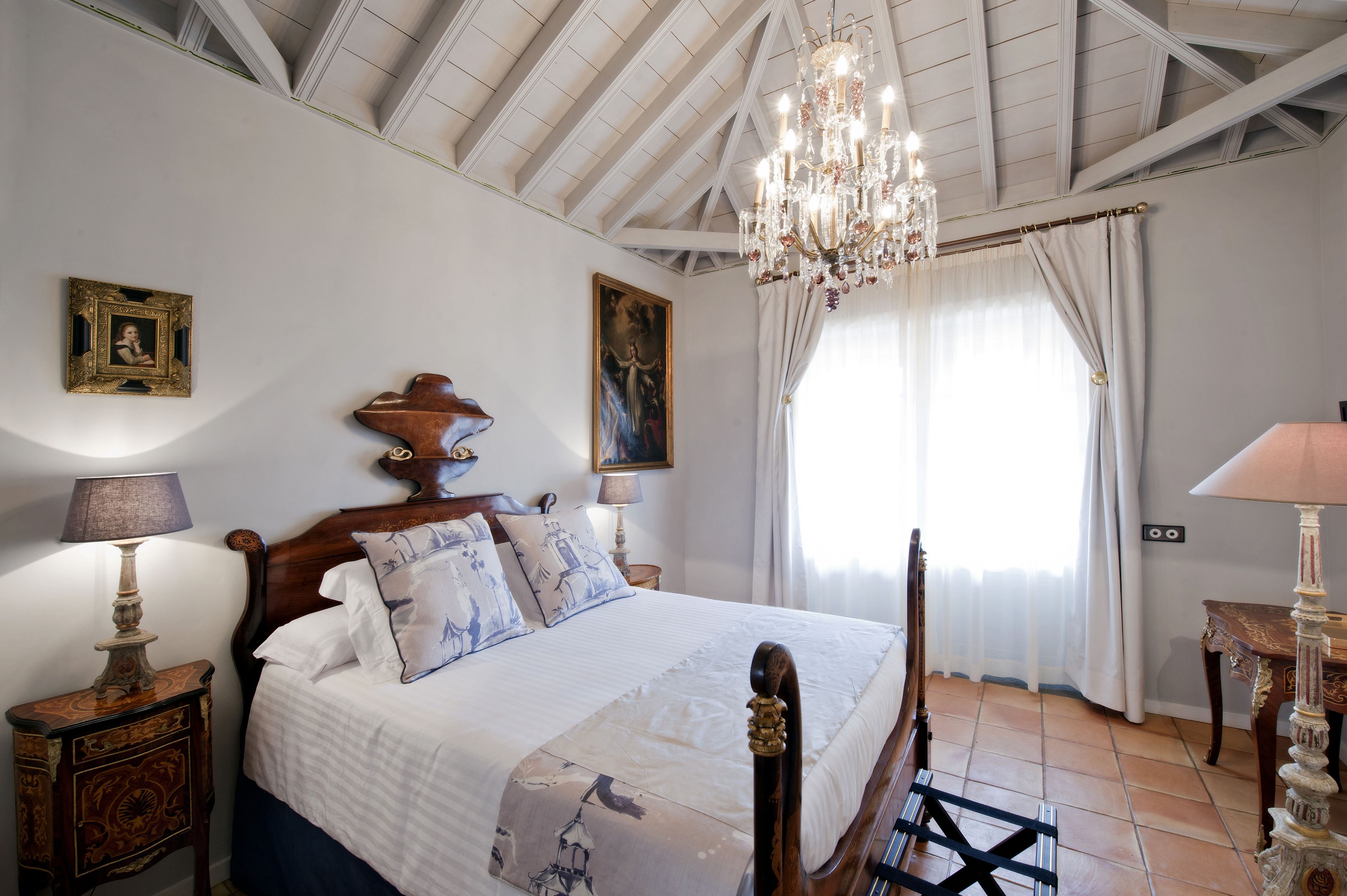 Une chambre à coucher avec un lit en bois, un lustre, une table de chevet, une lampe et un tableau au mur.