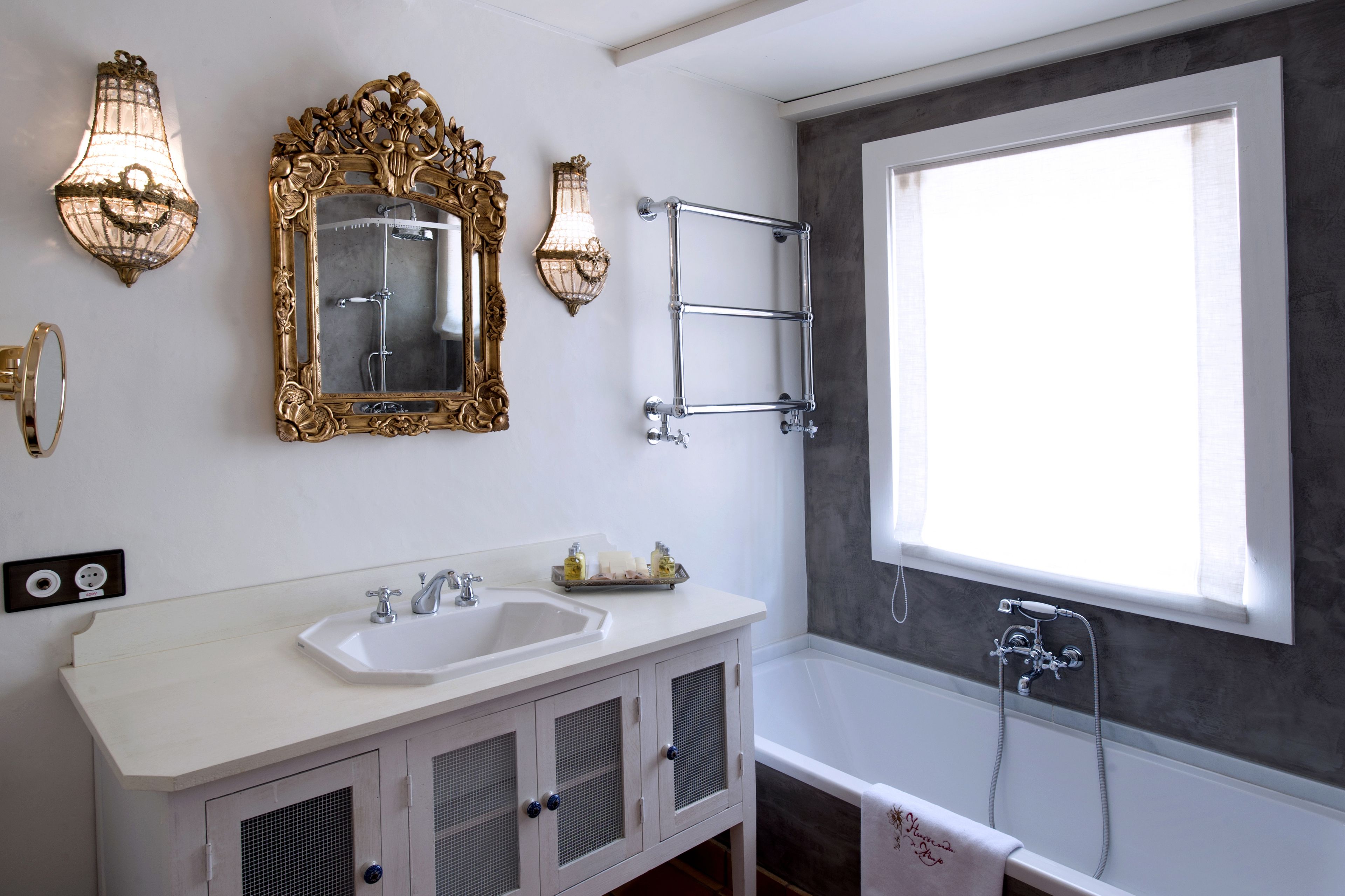 Une salle de bain avec un lavabo blanc, deux appliques murales, un grand miroir et une baignoire.