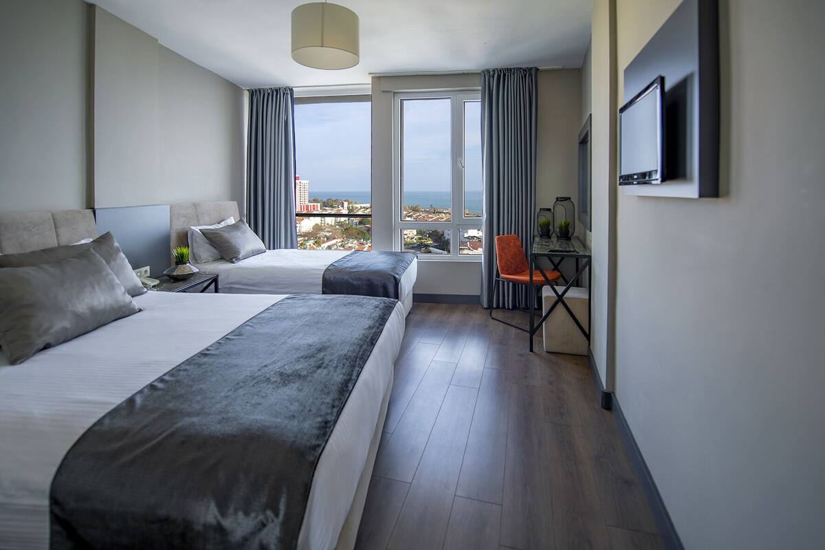 A modern hotel room with two beds, a desk, and a TV.