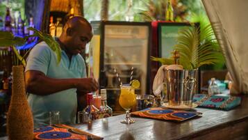 Zona de bar con un bartender preparando una bebida, una copa de cóctel con una rodaja de limón y una variedad de botellas y utensilios de bar sobre la barra.