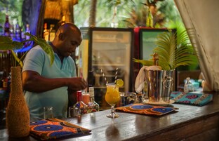 Zona de bar con un bartender preparando una bebida, una copa de cóctel con una rodaja de limón y una variedad de botellas y utensilios de bar sobre la barra.