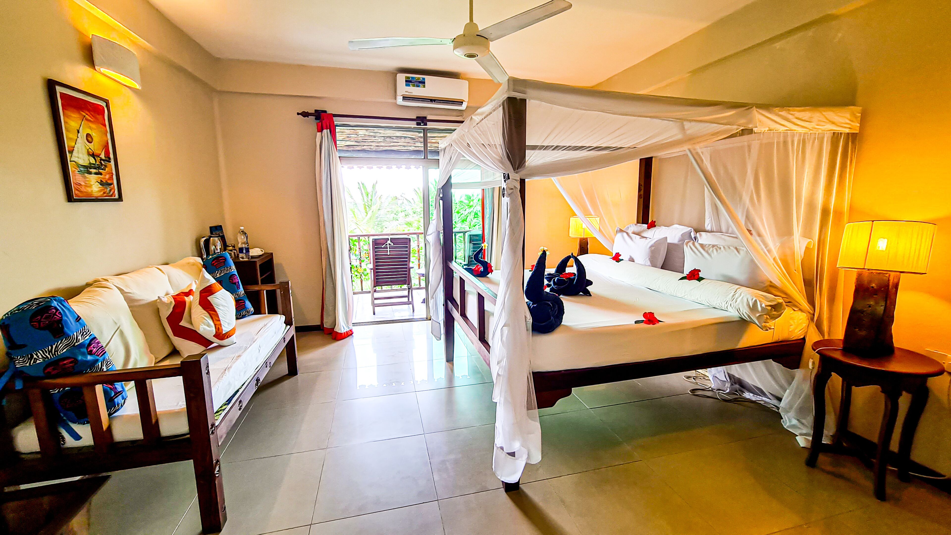 A spacious room with a four-poster bed, a sitting area with a sofa, and a balcony with a view.