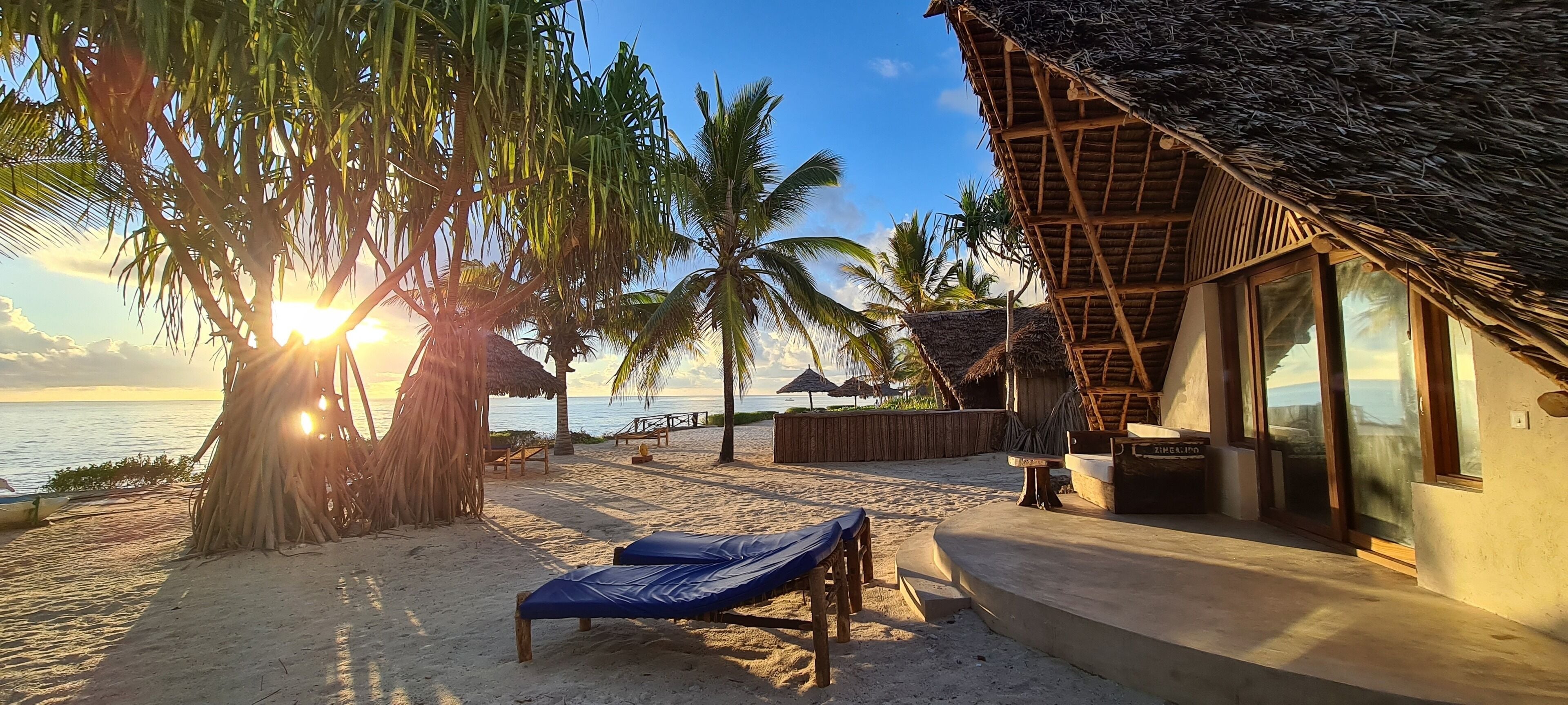 A beachside resort with thatched-roof huts, lounge chairs, and a view of the ocean.