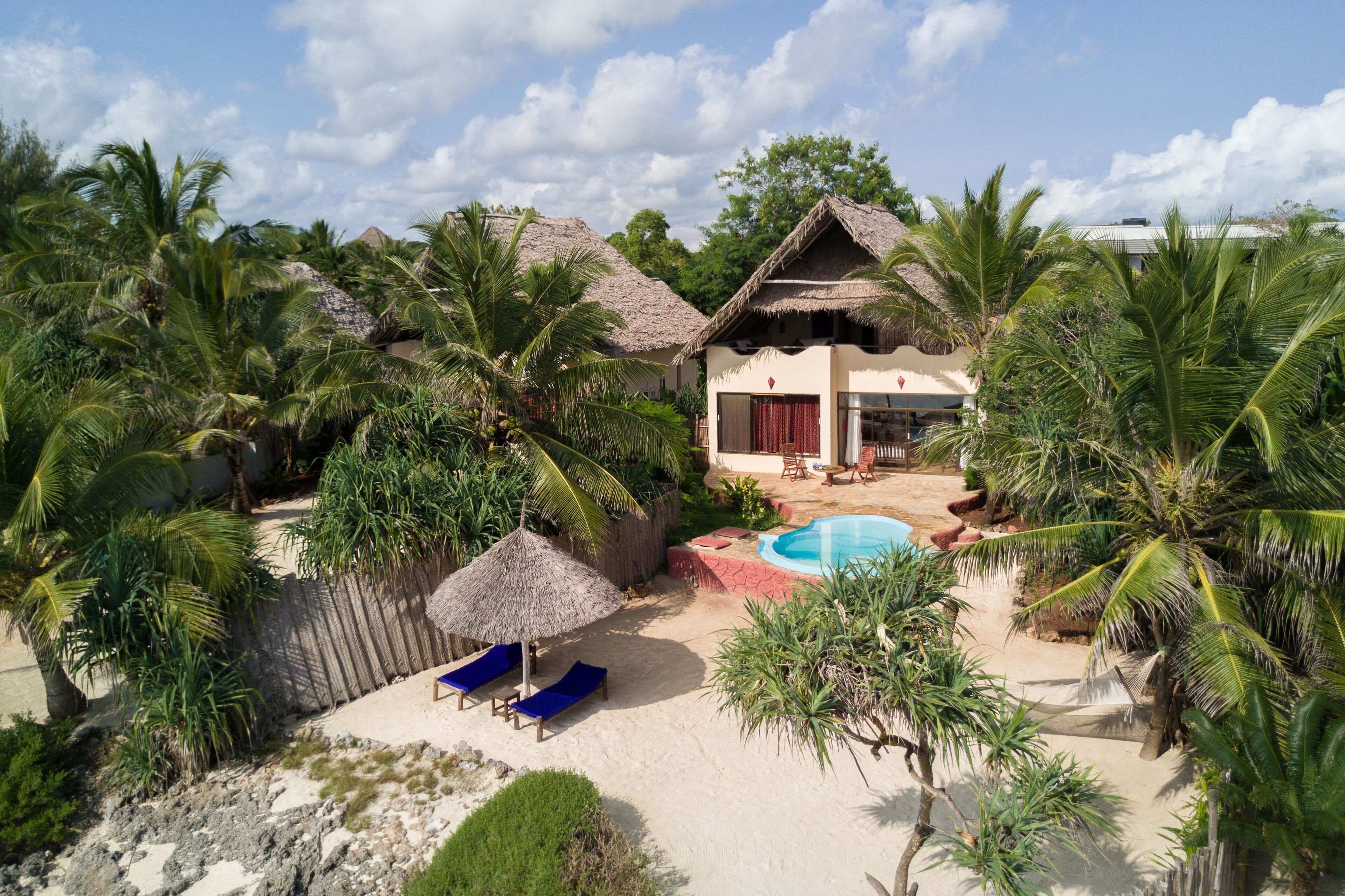 A tropical resort with a pool, thatched-roof buildings, and palm trees.