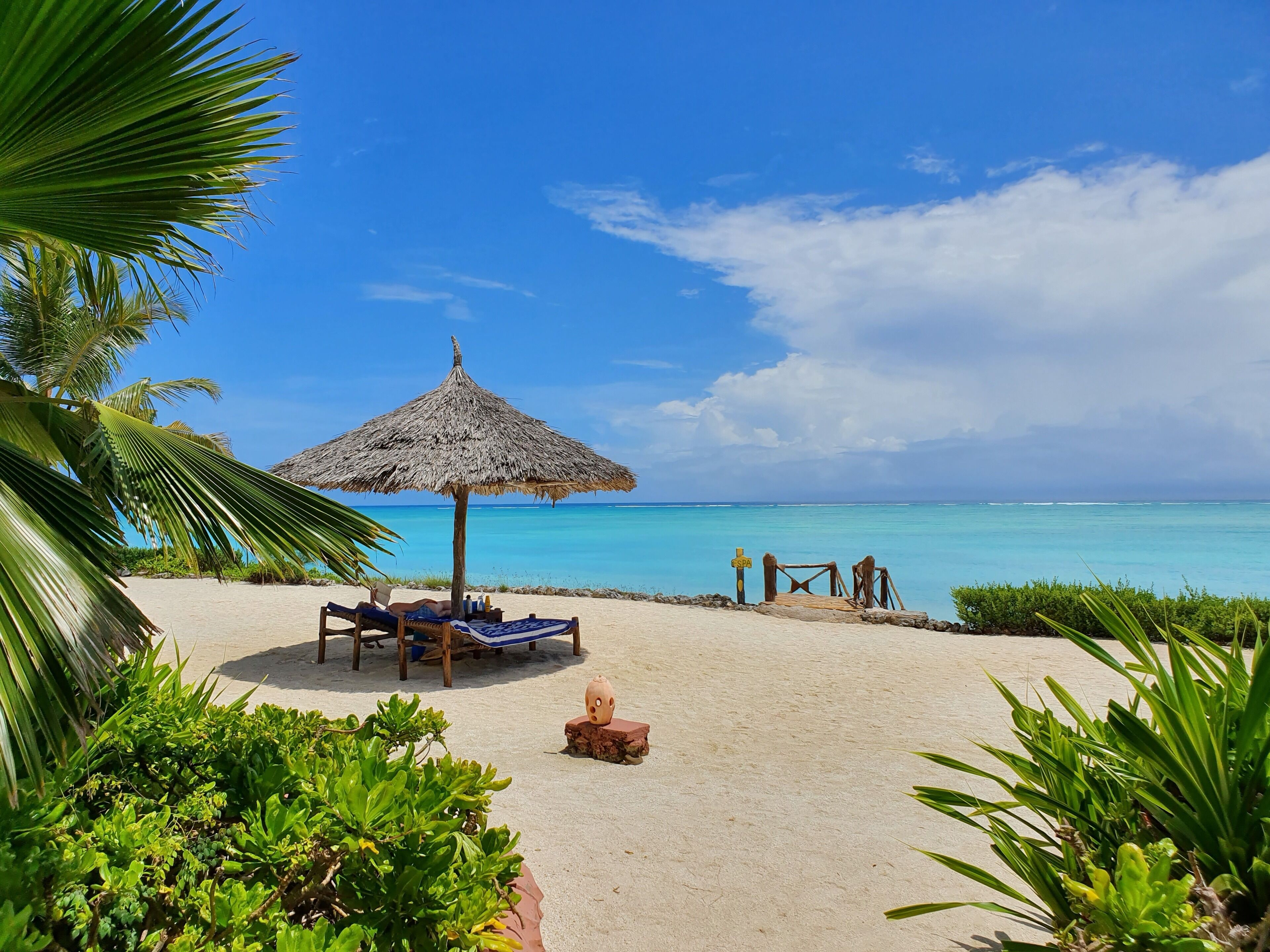 A beach with a thatched umbrella, lounge chairs, and a sign indicating a spa.